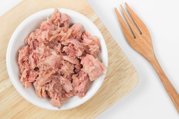bowl of tuna chunks on wood plate with wood fork on white background. 