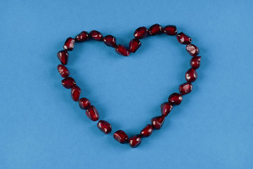 Obraz premium Pomegranate seeds shaped as heart on blue paper background. Love card concept, Valentine's day theme