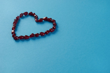 Pomegranate seeds shaped as heart on blue paper background. Love card concept with copy space, Valentine's day theme