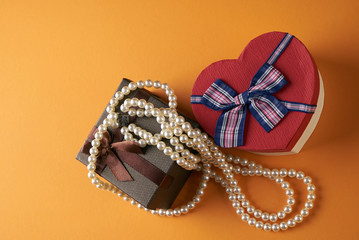 Pearl necklace with heart shaped gift box on a orange background, Love present card concept. Valentine's day theme