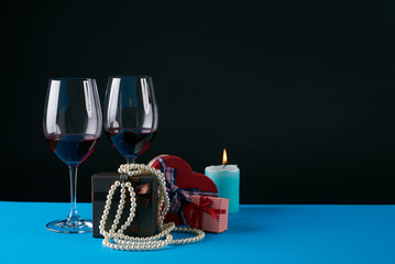Two wine glasses with gift boxes, candle and pearl necklace on dark background. Love present card concept with copy space. Valentine's day theme