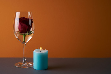 Wineglass with rosebud inside, candle and heart on orange background. Love card concept with copy space. Valentine's day theme