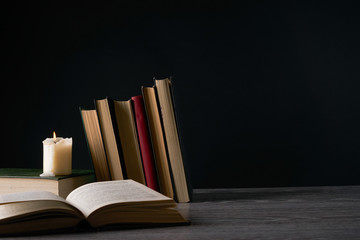 Books and candle on wooden table against dark background. Education, knowledge concept with copy space