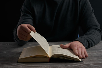 Man flipping page, reading book on a wooden table