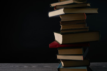 Stack of books on wooden table against black background. Education concept with copy space