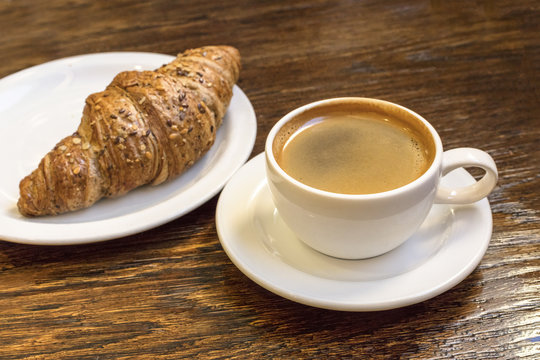 Cup of dark coffee with cereal croissant