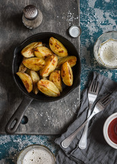 Baked potatoes in a cast iron frying pan and two glasses of beer on wooden background, top view