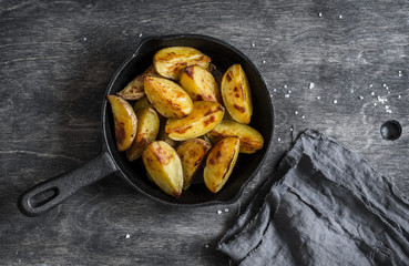 Baked potatoes in a cast iron skillet on wooden background, top view