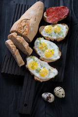 Bruschettas with fried quail eggs over black wooden background