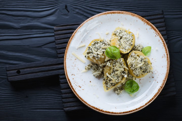 Plate with cheese and spinach conchiglioni, black wooden surface