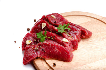 Pieces of meat with garlic and parsley on wooden board isolated. Raw beef. Top view.