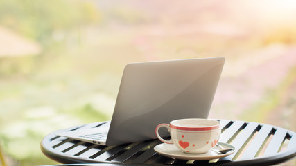 Laptop and white coffee cup on desk in flowers garden background