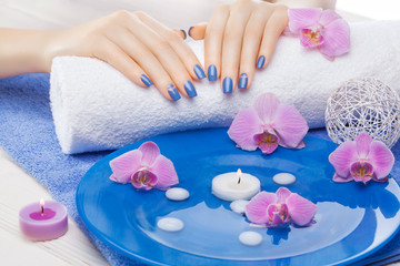 Obraz na płótnie Canvas beautiful blue manicure with orchid and towel on the white wooden table. spa