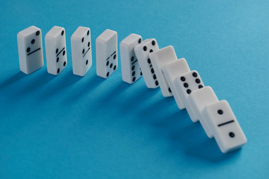 White toppling domino play pieces on blue background. Chain reaction