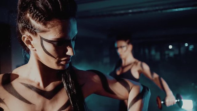 Two young athletes, muscular women training in the gym with weights close up