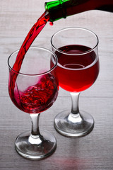 glass of red wine. Wine is poured into a glass from bottle on a light wooden background