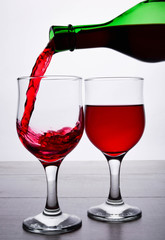 glass of red wine. Wine is poured into a glass from bottle on a light wooden background