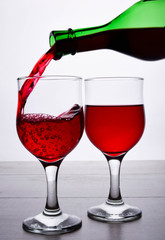 glass of red wine. Wine is poured into a glass from bottle on a light wooden background