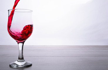 glass of red wine. Wine is poured into a glass from bottle on a light wooden background