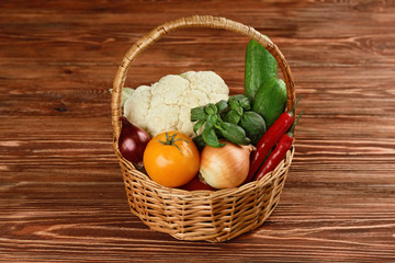 Fresh vegetables in wicker basket on wooden background
