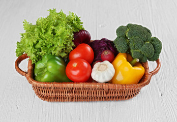 Fresh vegetables in wicker basket on wooden background