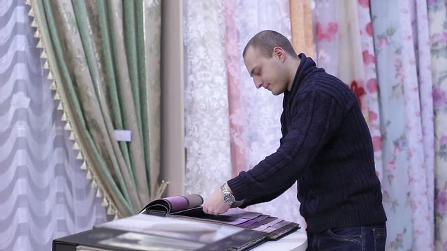 Young Man looks catalog of textile fabrics in the store