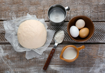 Fresh dough, eggs and milk on wooden background