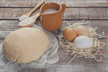 Fresh dough, eggs and milk on wooden background