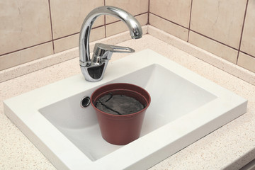 Water shortage concept. Pot with dry ground in white sink