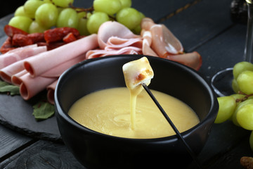 Gourmet Swiss fondue dinner on a winter evening with assorted cheeses on a board alongside a heated pot of cheese fondue with two forks dipping bread and white wine behind in a tavern or restaurant