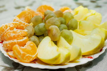a lot of fruit on a plate. Apple, tangerine, grapes.