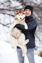 man playing with red siberian husky dog in snowy park