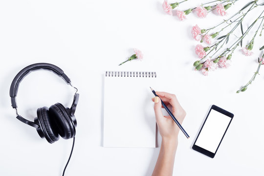 Female hand writing in a notebook, mobile phone, headset and flo