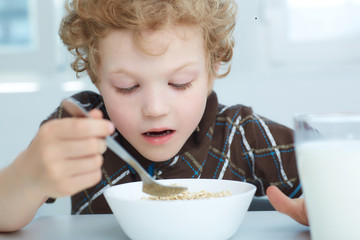 Boy eating cereal while having breakfast  in the kitchen.