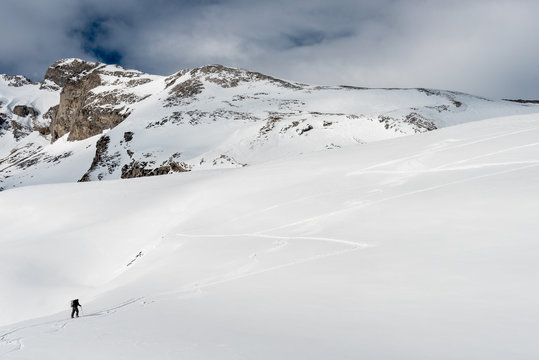 FORMIGAL, SPAIN - JUNE 20, 2017:  a mountain skier walks ahead using his skis and skins through a snowy valley in the vicinity of Formigal, Tena Valley, Spanish Pyrenees.