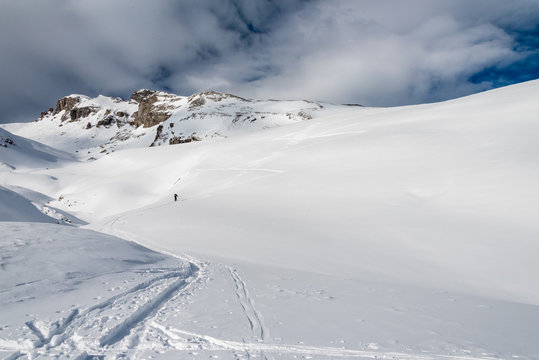 FORMIGAL, SPAIN - JUNE 20, 2017:  a mountain skier walks ahead using his skis and skins through a snowy valley in the vicinity of Formigal, Tena Valley, Spanish Pyrenees.