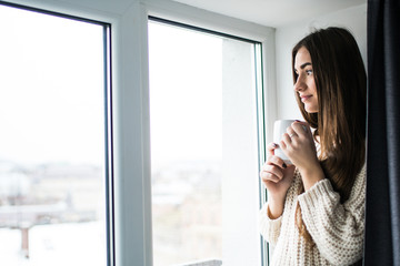 Woman in the morning. Attractive sexy woman with neat body is holding a cup with hot tea or coffee and looking at the window