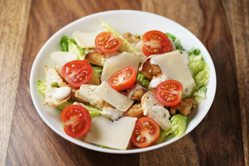 fresh homemade caesar salad with chicken and cherry tomatoes on wood table, shallow depth of field