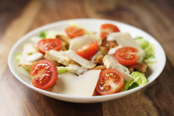 fresh homemade caesar salad with chicken and cherry tomatoes on wood table, shallow depth of field