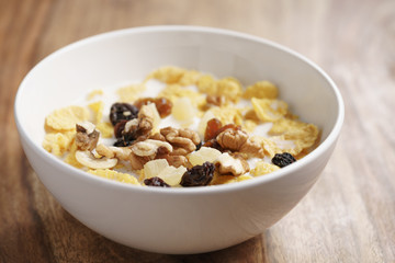 closeup photo of corn flakes with fruits and nuts in white bowl on wood table, simple healthy breakfast