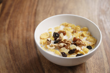 corn flakes with fruits and nuts in white bowl on wood table with copy space, healthy food