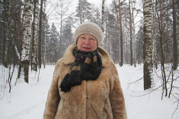 Portrait of senior woman fur coat and hat standing in cold winter snow covered forest