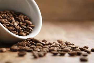 overturned cappuccino cup with roasted coffee beans on wood table, with copy space