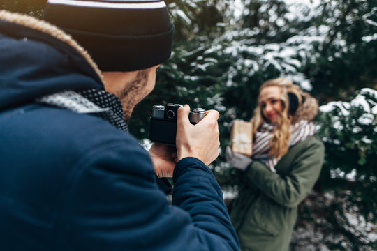 A young man in a blue jacket photographing woman with a gift in retro camera in winter Park
