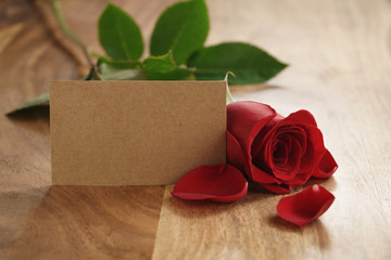 beautiful red rose with petals and empty paper card on old wood table, romantic background with copy space