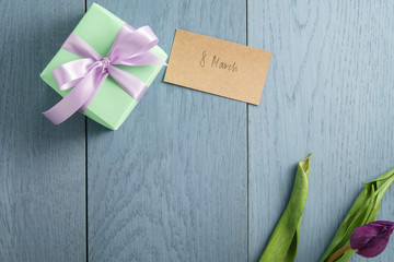 green gift box on blue wood table with paper card for 8 march, top view