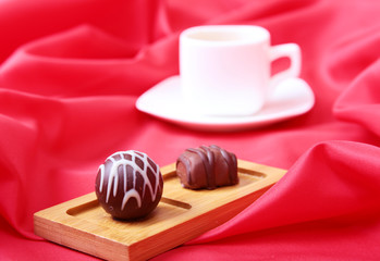 White cup of coffee and cognac in a glasses, pralines on red background.