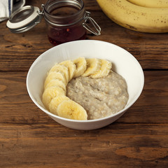 Bowl of oatmeal porridge with banana and jam on wooden background, healthy breakfast , diet food. Instagram size