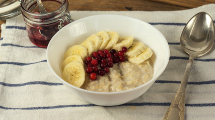 Bowl of oatmeal porridge with banana, berries and jam on wooden background, healthy breakfast , diet food
