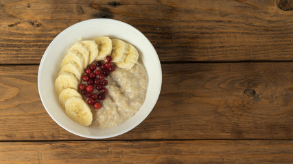 Bowl of oatmeal porridge with banana, berries and jam on wooden background, healthy breakfast , diet food